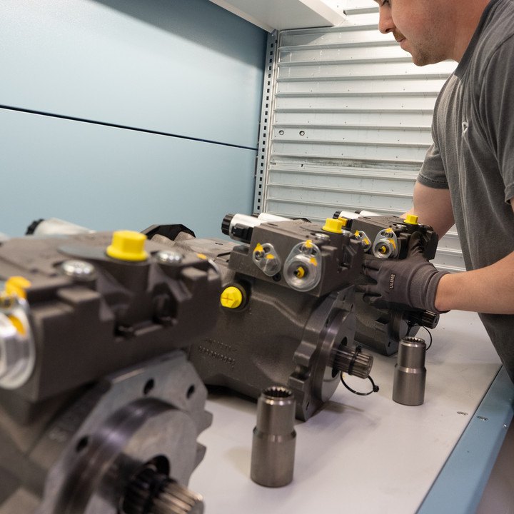 A Lifco technician in gloves handling three new Linde hydraulic pumps on a white workbench